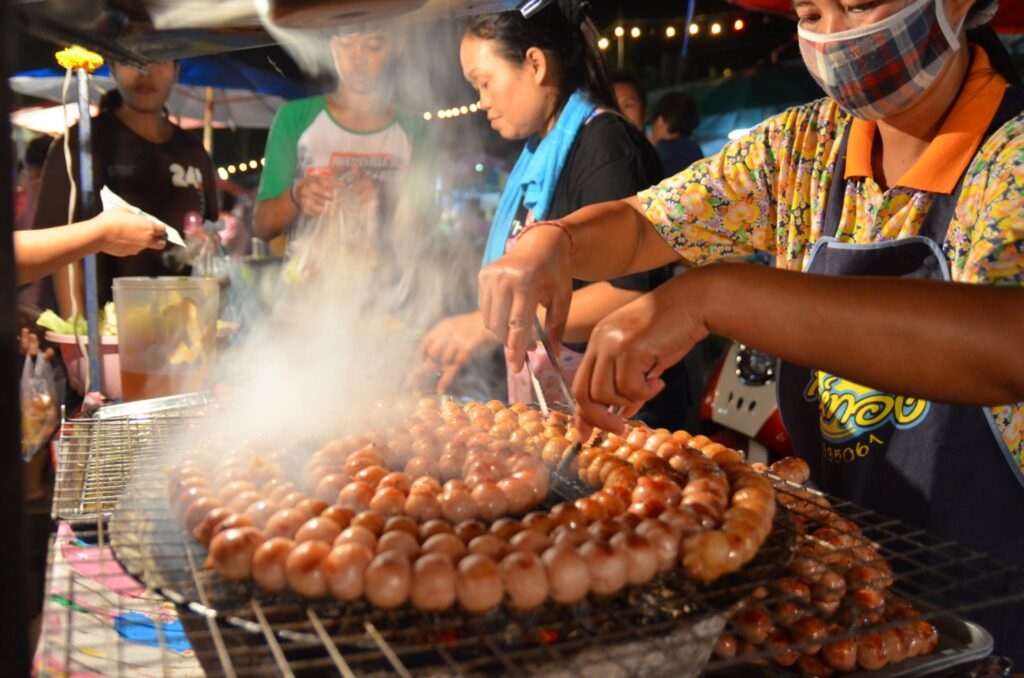 A woman grilling sai krok isaan, a Thai sour sausage from the northeast of Thailand.